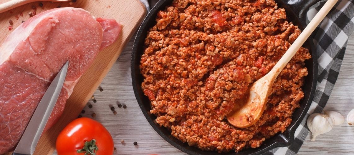 Bolognese sauce cooking in a frying pan and ingredients on the table. horizontal view from above